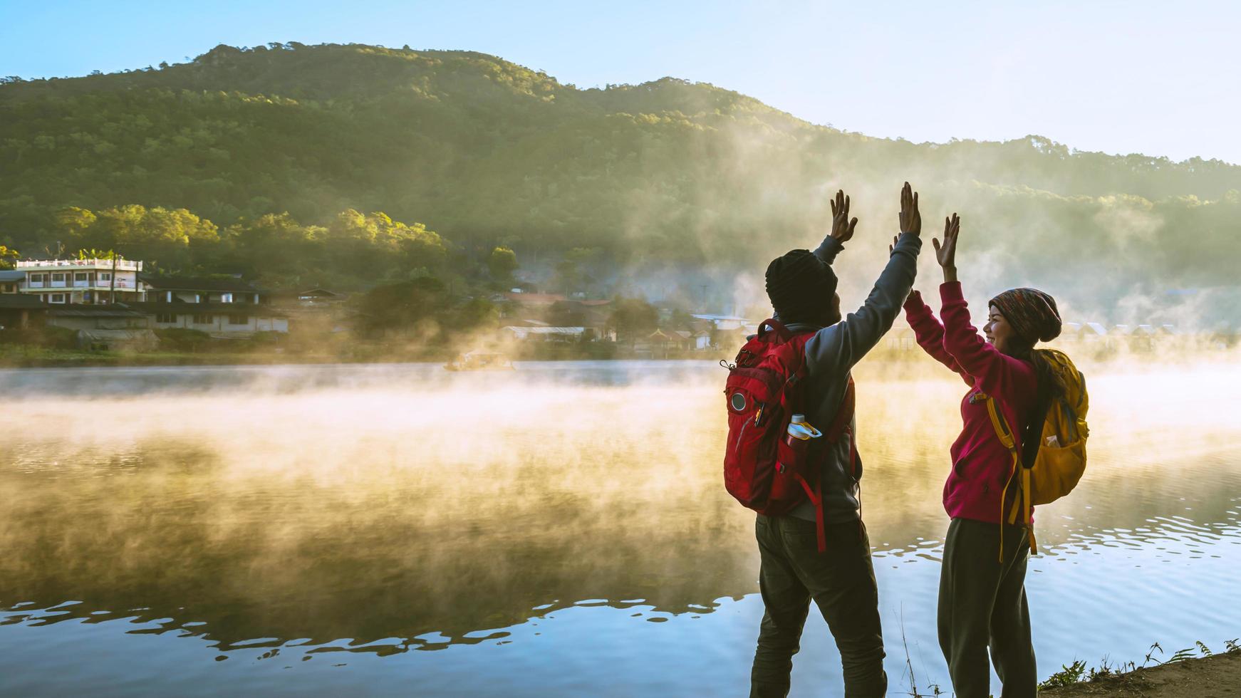 donna asiatica e uomo asiatico che viaggiava con lo zaino in piedi vicino al lago, sorrideva, felice e si godeva la bellezza naturale della nebbia. foto