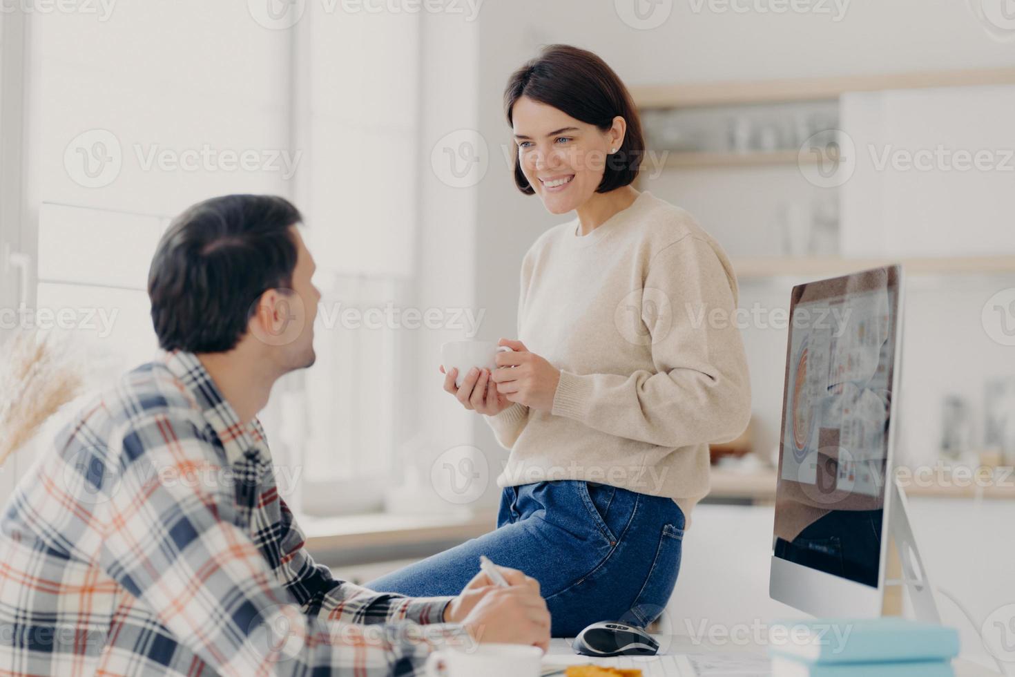 coppia di famiglia discute di fare investimenti futuri, posa in uno spazio di coworking, lavora su un computer moderno, guarda felicemente l'un l'altro durante la pausa caffè, vuole fare acquisti, lavorare da remoto a casa foto