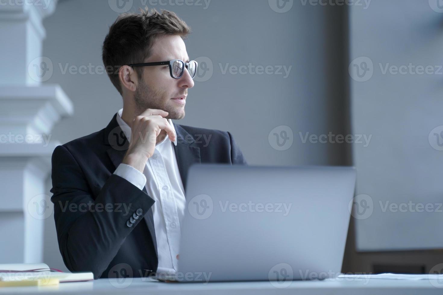 il giovane impiegato maschio tedesco concentrato si siede alla scrivania nel posto di lavoro di casa distratto dallo schermo del laptop foto