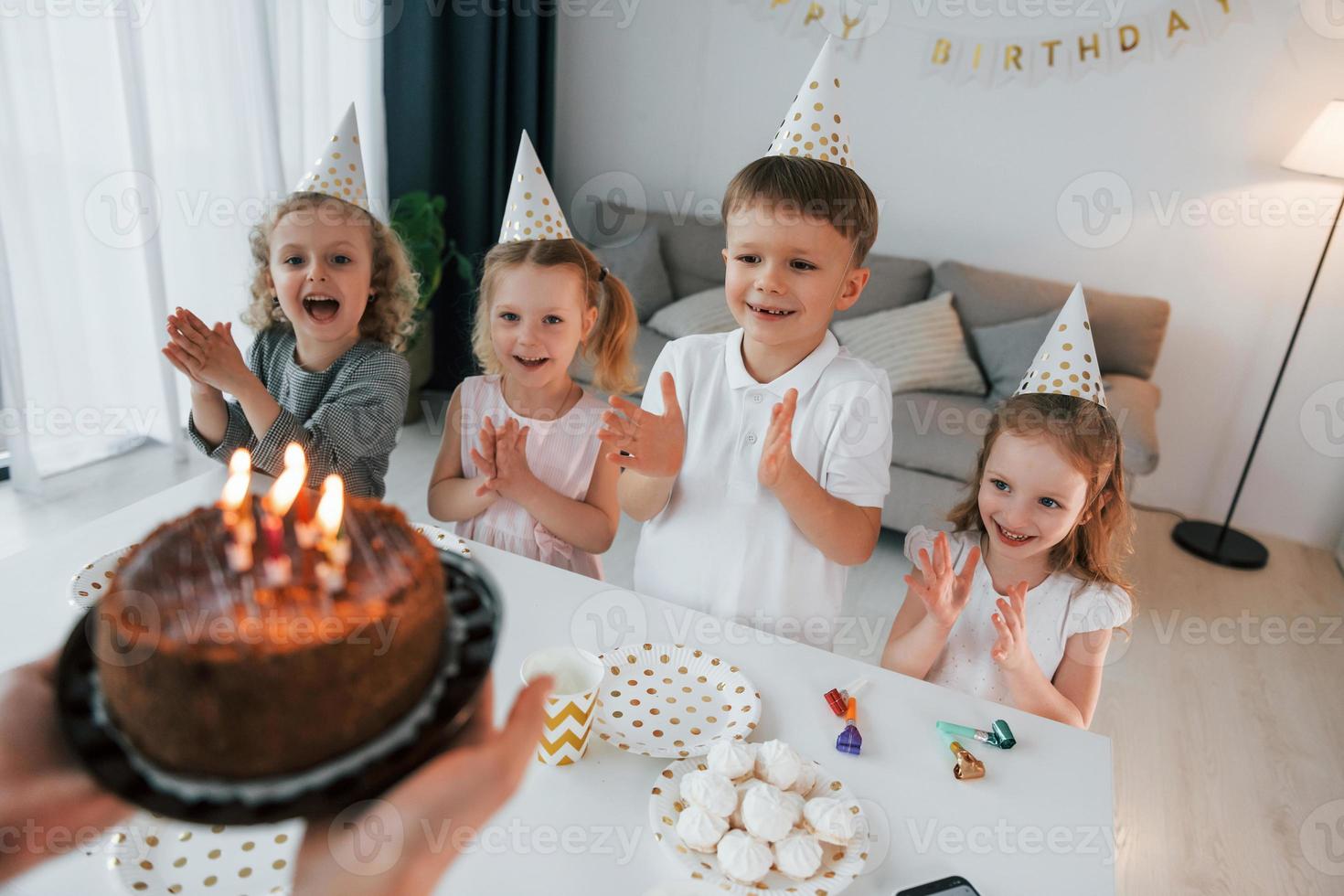 donna che tiene la torta con le candele. festeggiare il compleanno. gruppo di bambini è insieme a casa durante il giorno foto