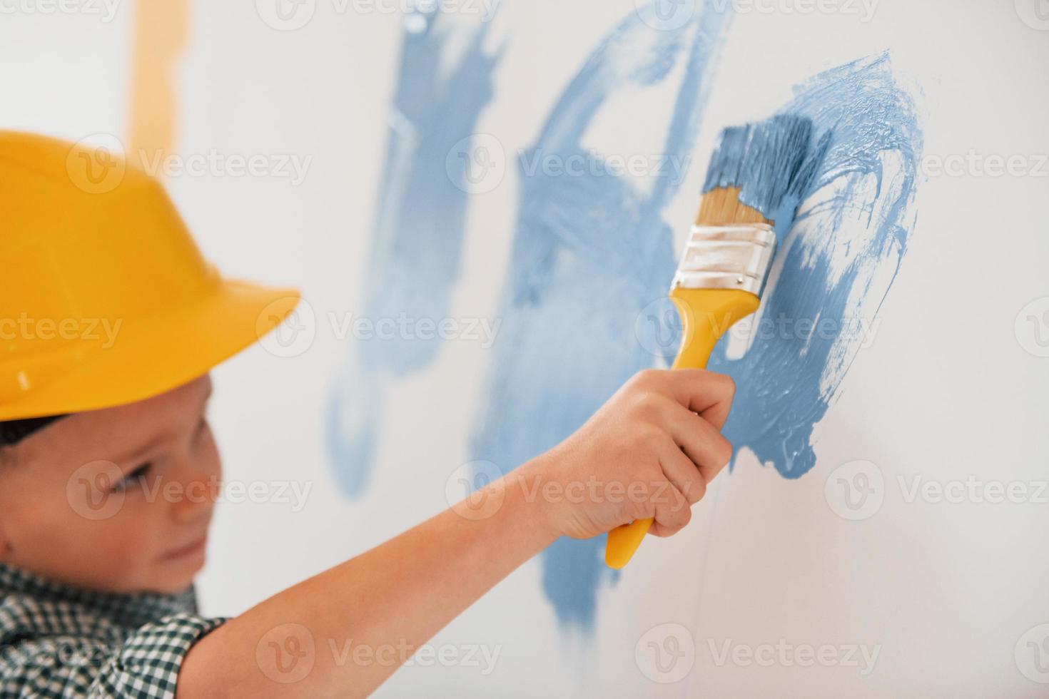 utilizzando i colori blu e giallo. ragazzino che dipinge pareti nella stanza domestica foto