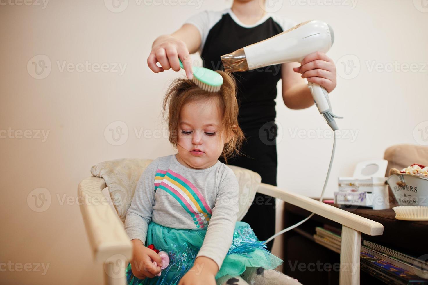 mamma con la figlia del bambino che fanno insieme la routine quotidiana. la madre sta spazzolando e asciugando i capelli del bambino dopo la doccia. foto