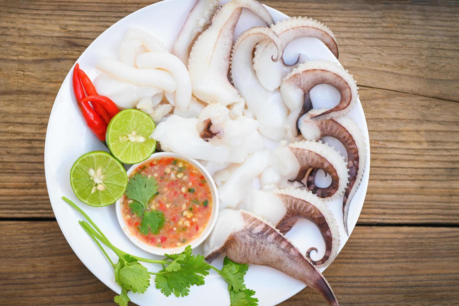 piatto di frutti di mare calamari su piatto bianco, calamari freschi cotti a vapore con insalata di verdure limone lime e salsa di frutti di mare salsa chili servire sul tavolo, tentacoli di polpo seppie gourmet dell'oceano foto