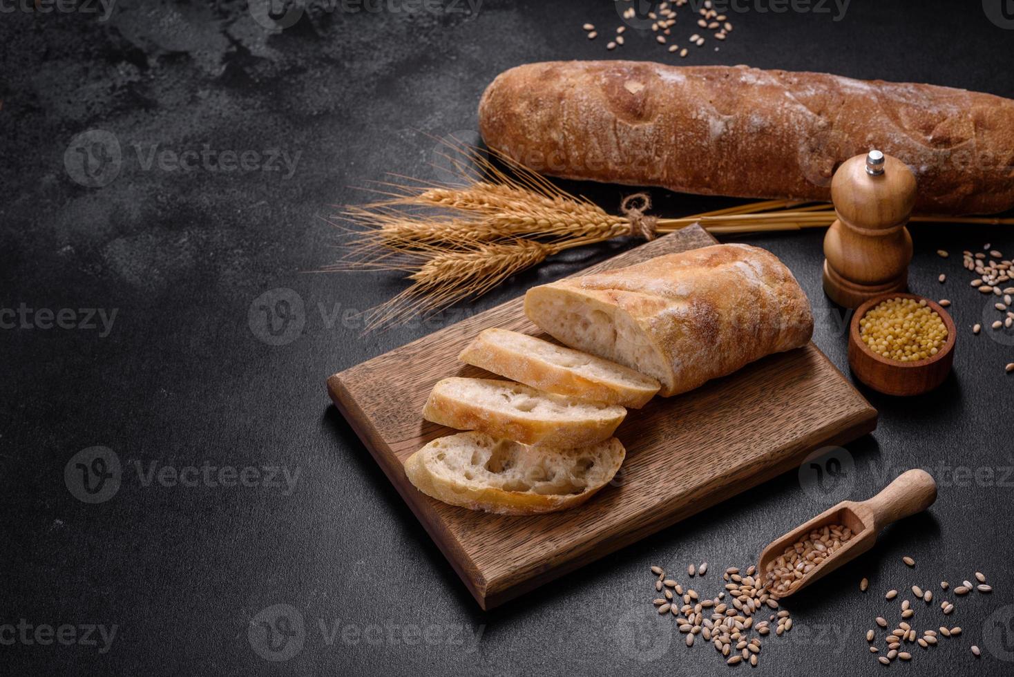 baguette francese tagliata a fette su un tagliere di legno su uno sfondo di cemento scuro foto