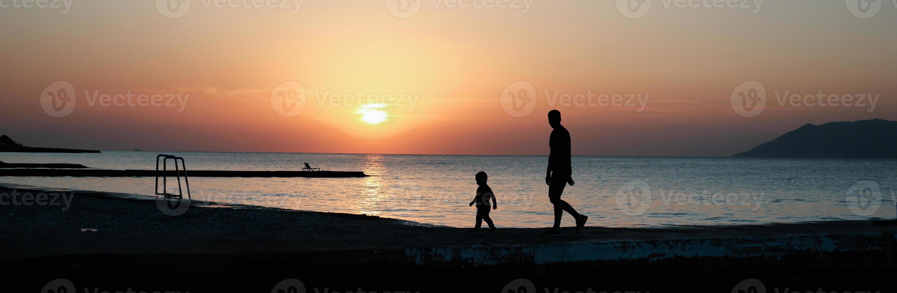 padre e figlio piccolo che camminano insieme in riva al mare. foto