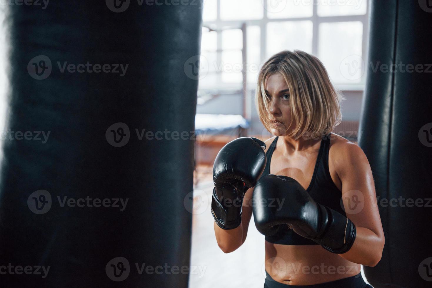 ritratto di bella donna. pugile femminile sta perforando il sacco. la bionda fa esercizio in palestra foto