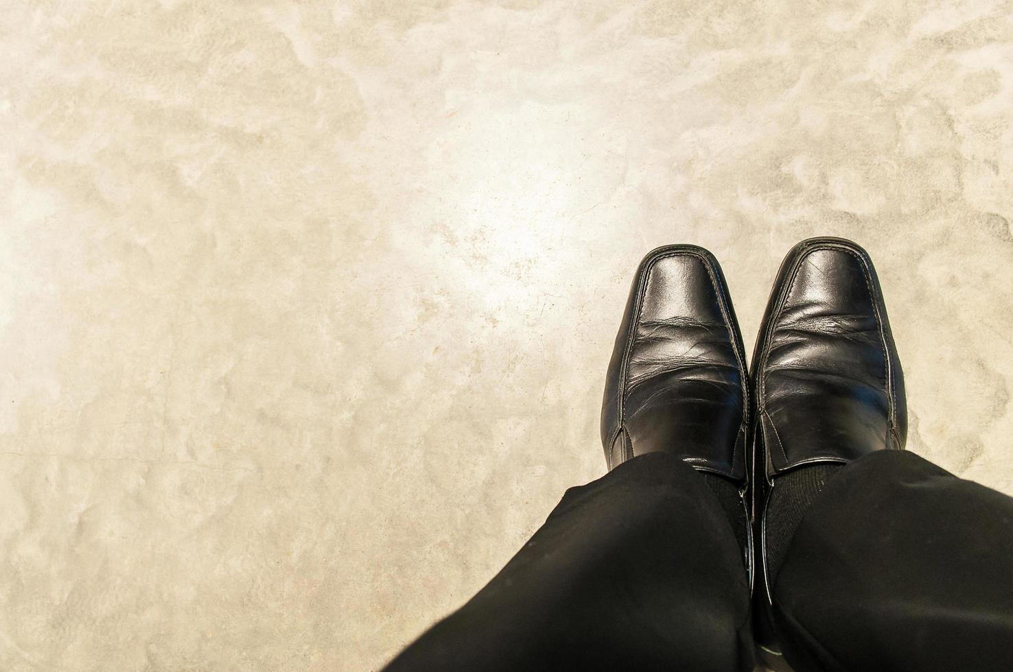 vista dall'alto di vecchi pantaloni neri e scarpe di pelle di relax seduto uomo d'affari sul pavimento di cemento. la foto è focalizzata sulle scarpe.