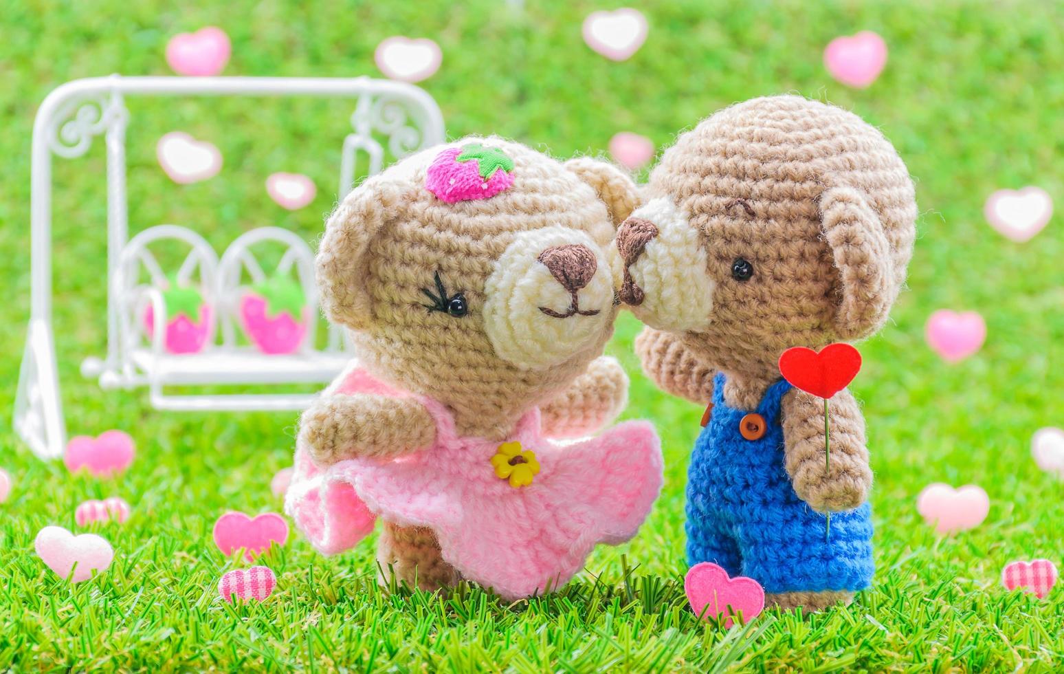 adorabile bacio bambino orsi bambola all'uncinetto su erba verde con altalena sfocata e sfondo del cuore. foto
