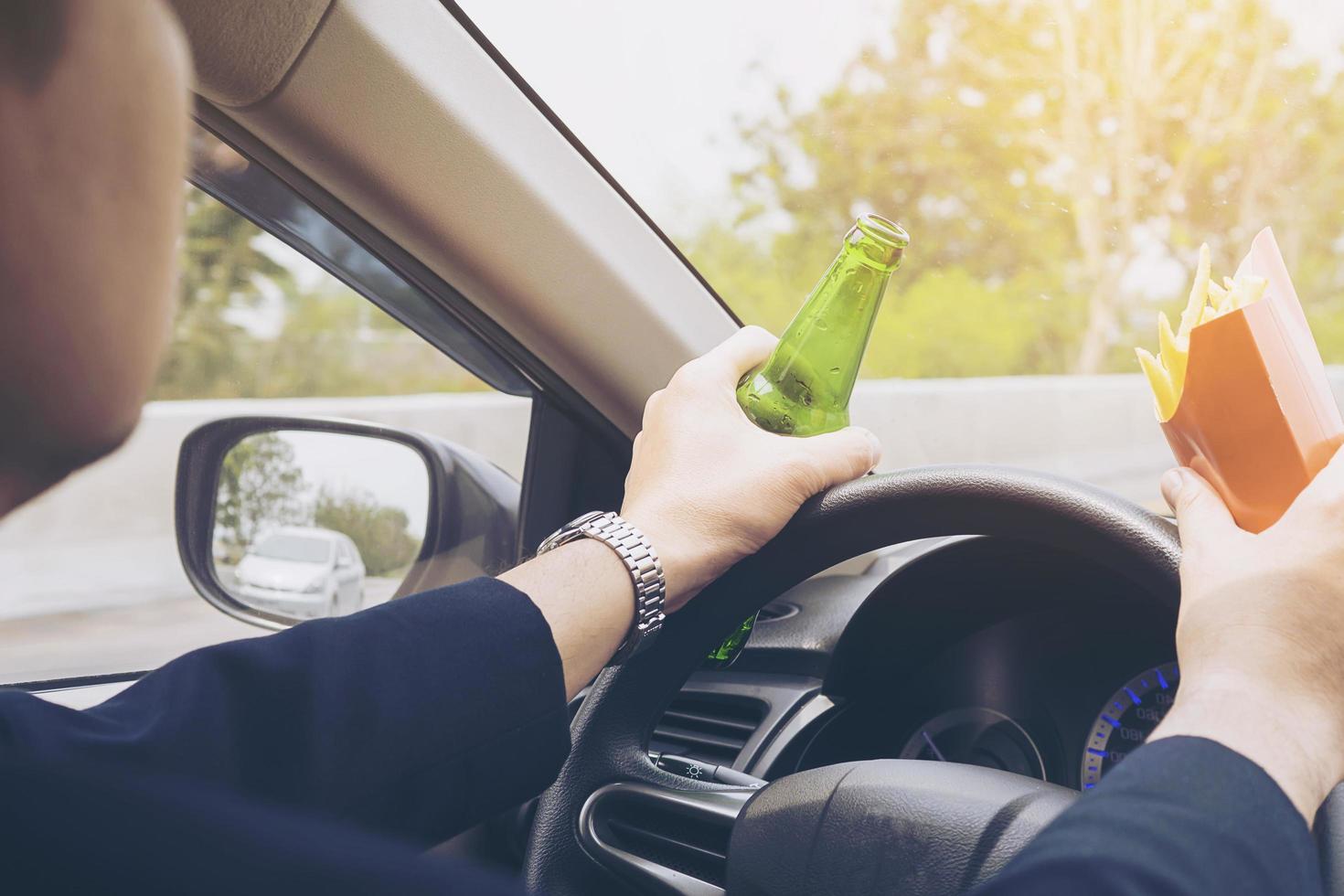 uomo che guida l'auto mentre mangia patatine fritte e birra foto