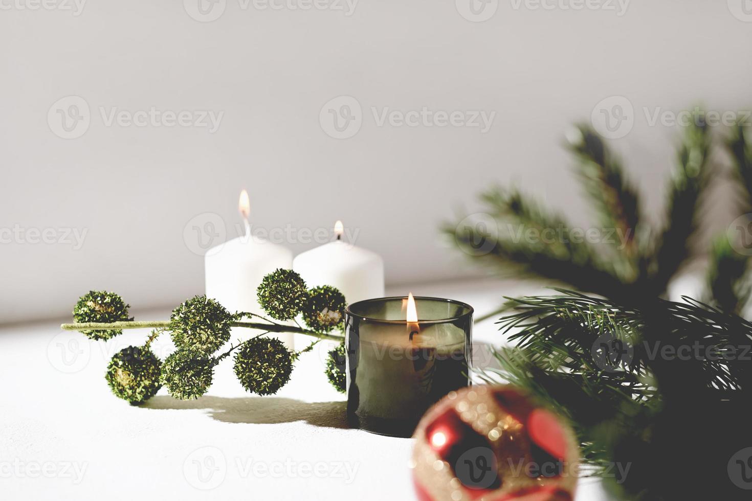 candela di Natale profumata verde e candele di cera bianca accanto al ramo di pino e palla di Natale rossa. selezione festiva. candela profumata di bosco e pino foto