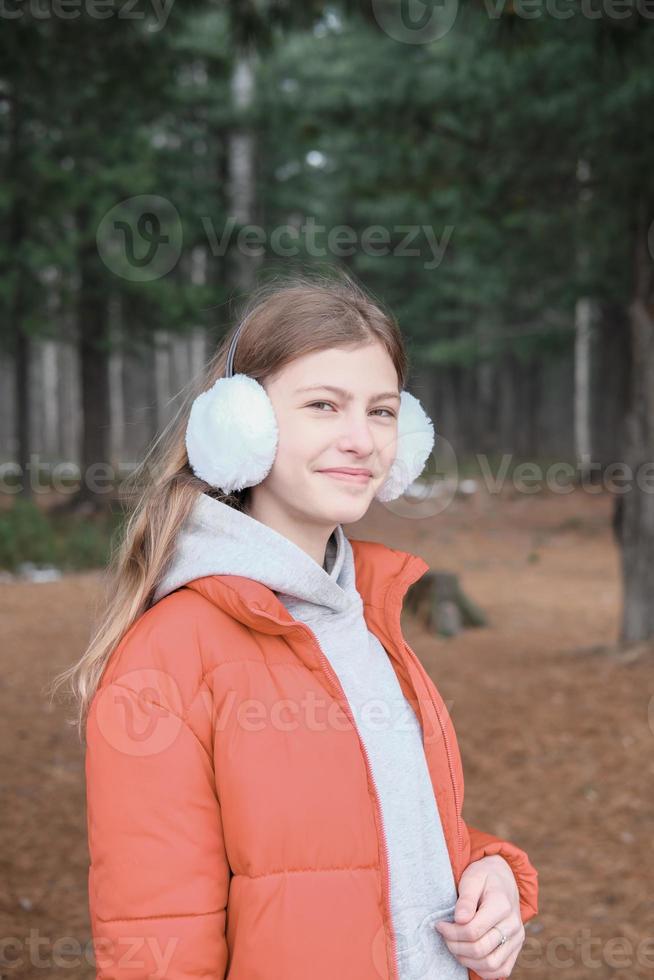 bella ragazza adolescente che indossa giacca rossa e cuffie che cammina nel parco. studentessa nella foresta. ragazza sorridente e guardando la fotocamera foto