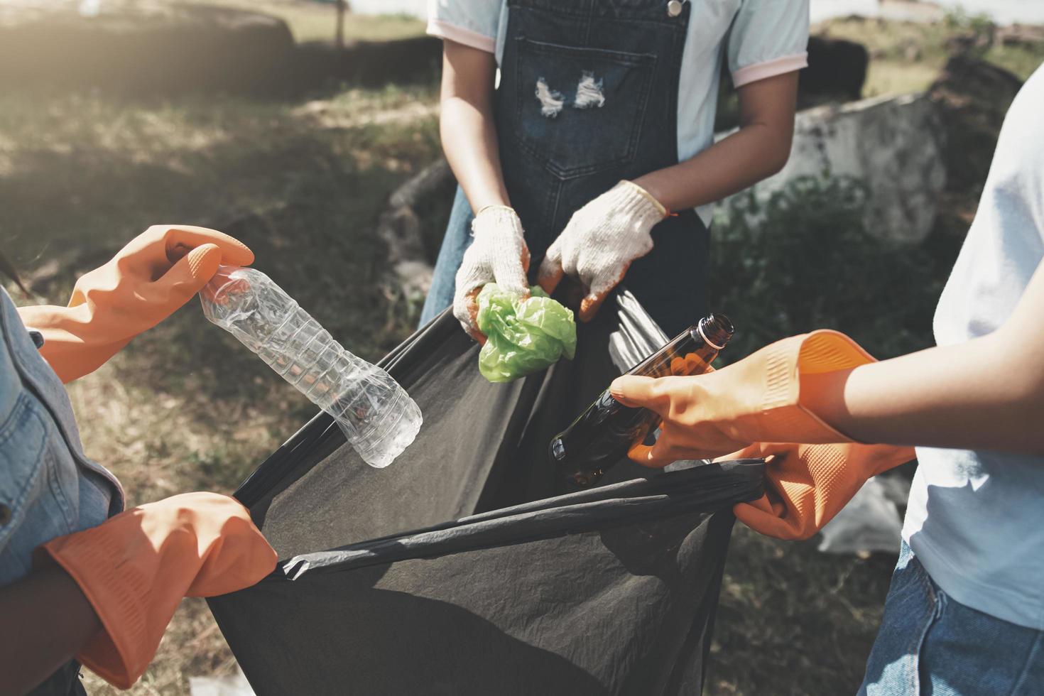 persone che raccolgono la spazzatura e la mettono in un sacchetto di plastica nera per la pulizia al parco foto