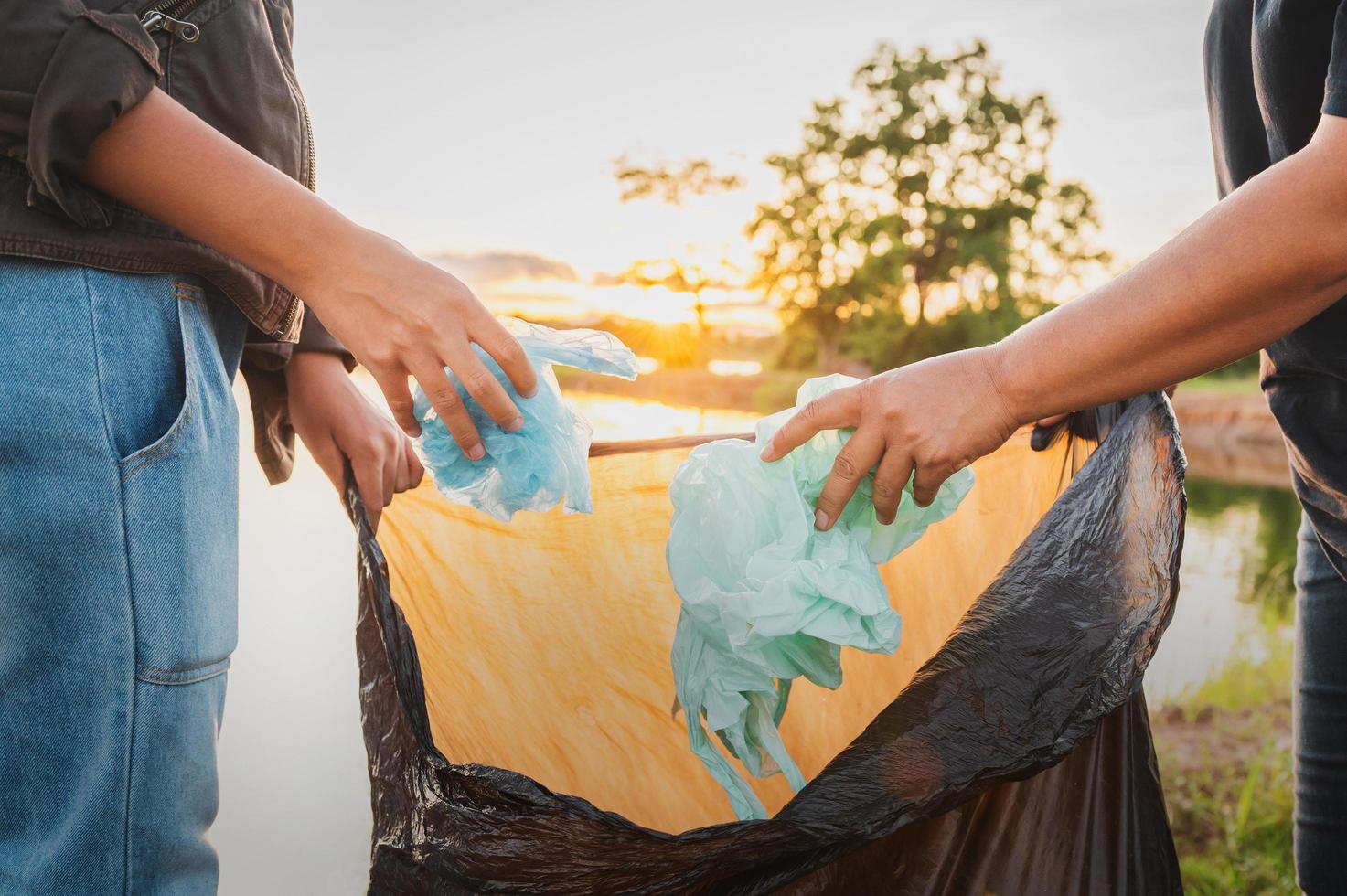 mano della donna che raccoglie il sacchetto di plastica dell'immondizia per la pulizia al parco foto