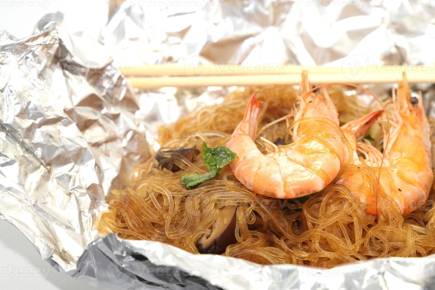 gamberetti al forno con spaghetti di vetro, un alimento tradizionale tailandese avvolto in carta freud trattata termicamente e bacchette, pronto da servire su uno sfondo bianco. foto