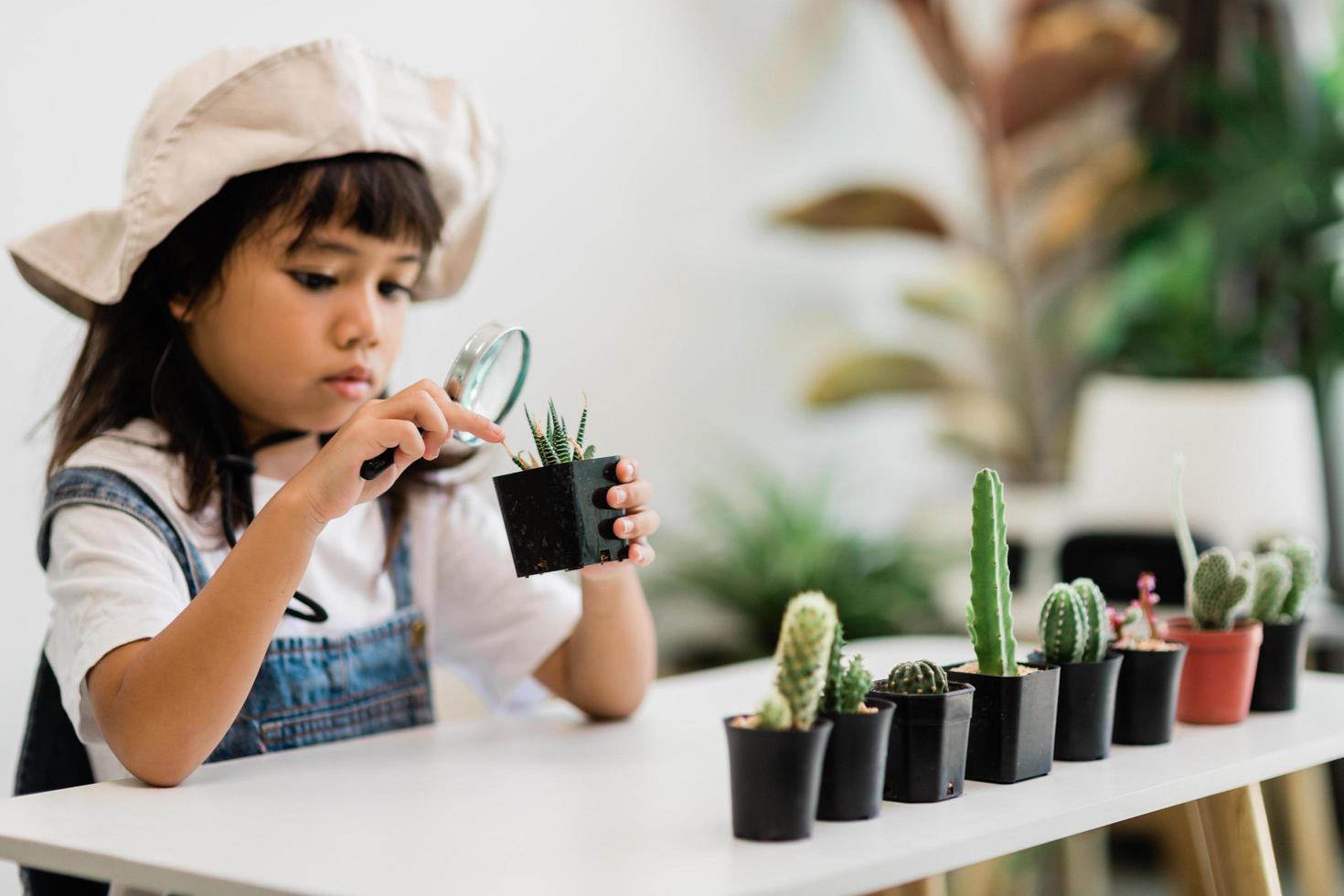 il bambino tocca delicatamente il nuovo stelo del cactus che cresce con cura, una mano tiene la lente d'ingrandimento. educazione della natura, montessori e concetto di abilità di osservazione. foto