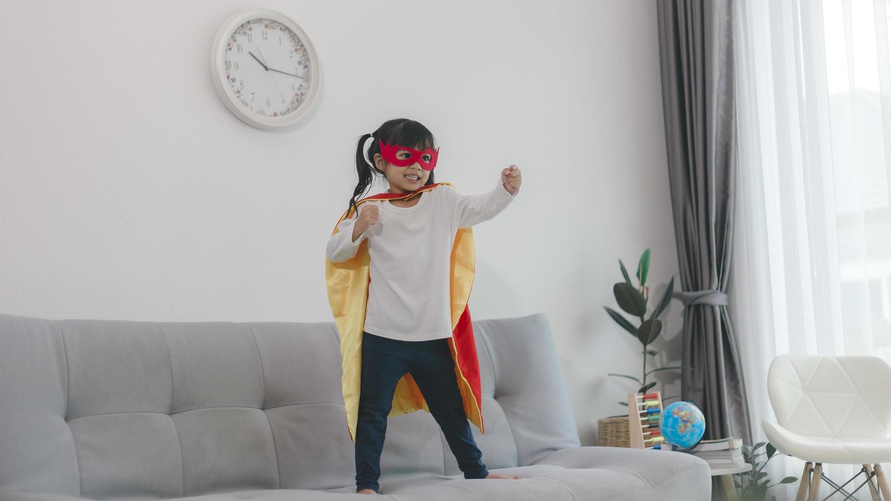 bambina in un costume da supereroe con maschera e mantello rosso a casa foto