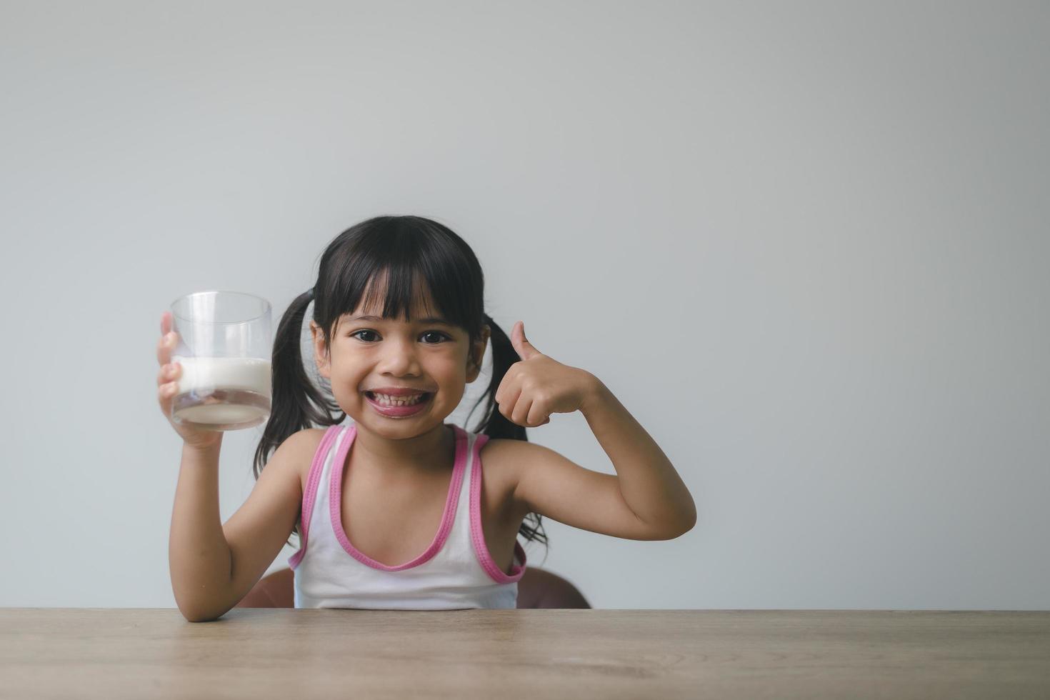 la bambina asiatica sta bevendo il latte da un bicchiere che era molto felice. foto