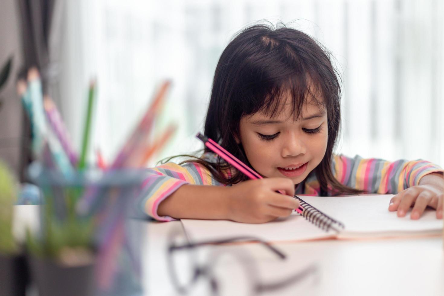 bambina che disegna sul suo libro e si diverte al tavolo da gioco. bambino che impara a colorare a casa o all'asilo. foto