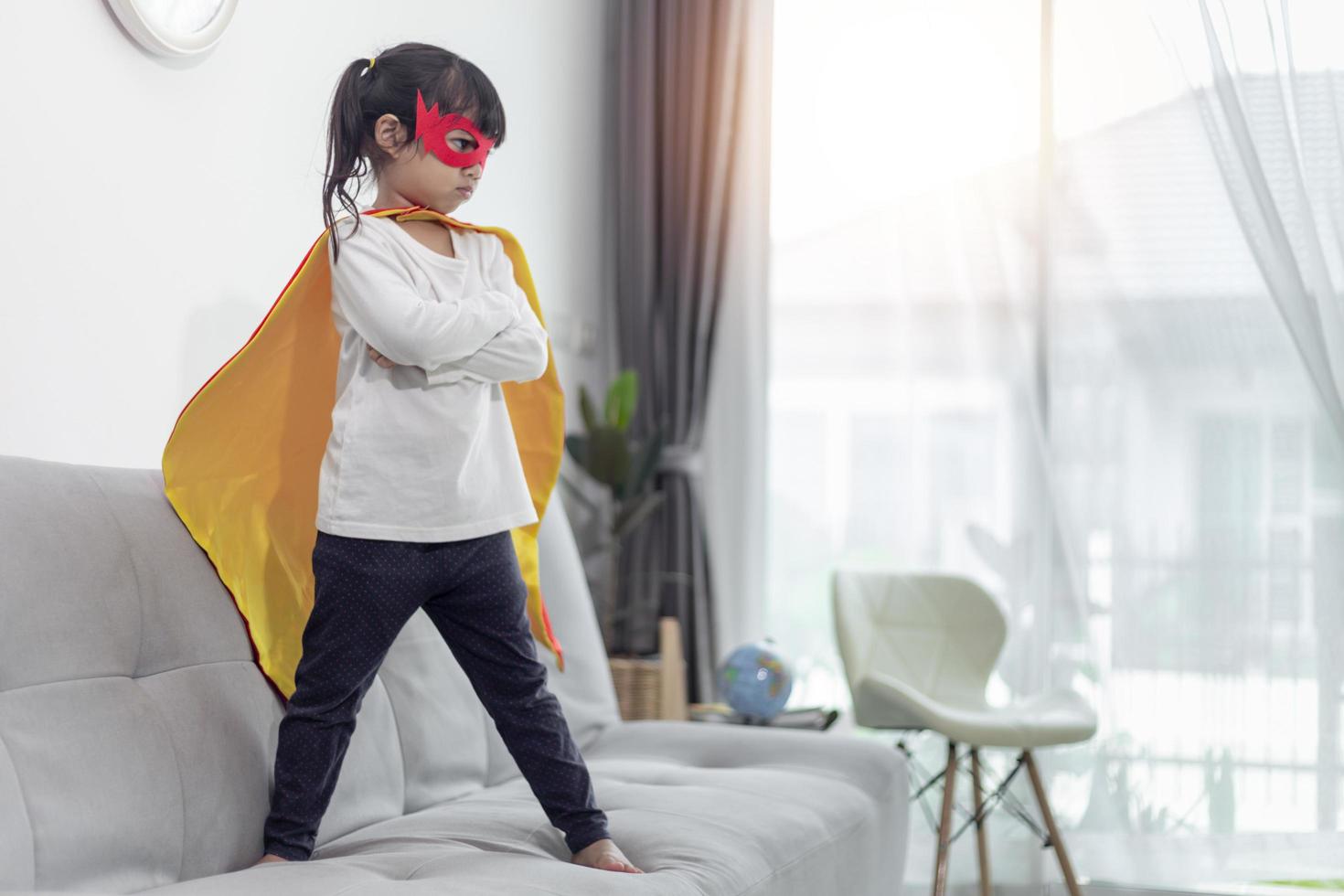 bambina in un costume da supereroe con maschera e mantello rosso a casa foto