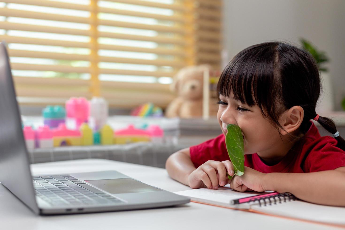 tempo di apprendimento. la scolaretta interessata con le cuffie si siede a casa e guarda la video lezione di istruzione. curiosa ragazza in età scolare pensa alla domanda dell'insegnante seleziona la risposta corretta sullo schermo del laptop foto