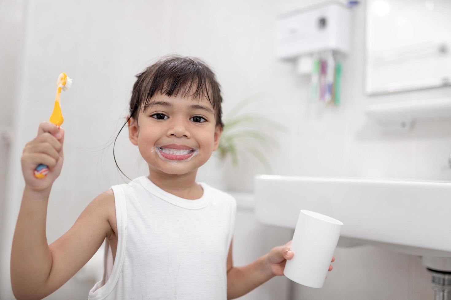 piccola neonata sveglia che si pulisce i denti con uno spazzolino da denti in bagno foto