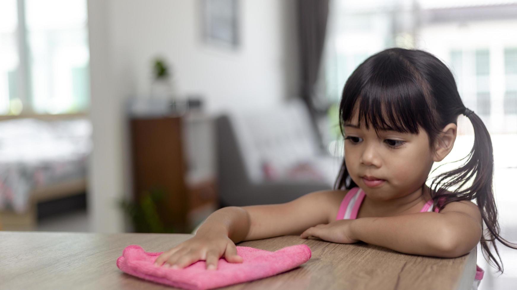 felice piccola ragazza asiatica che impara a pulire con uno straccio nel soggiorno di casa. concetto di lavoro domestico e domestico. foto