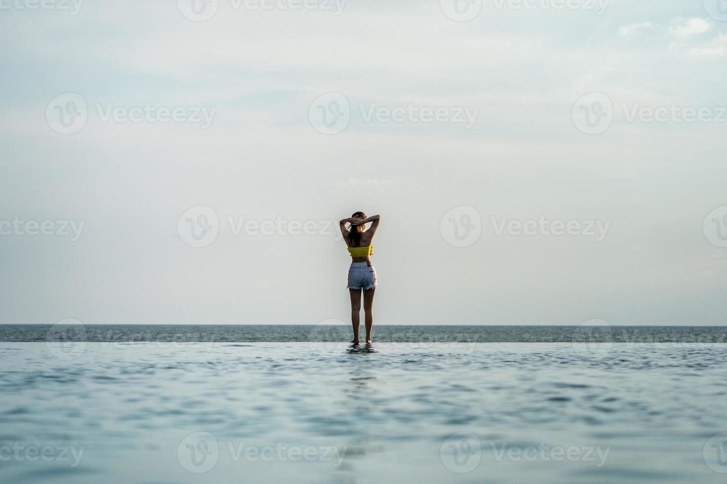 la femmina asiatica dell'adolescente tailandese in giallo si rilassa e il costume da bagno sta pubblicando sulla piscina a sfioro accanto alla spiaggia del mare nel resort della tailandia. foto