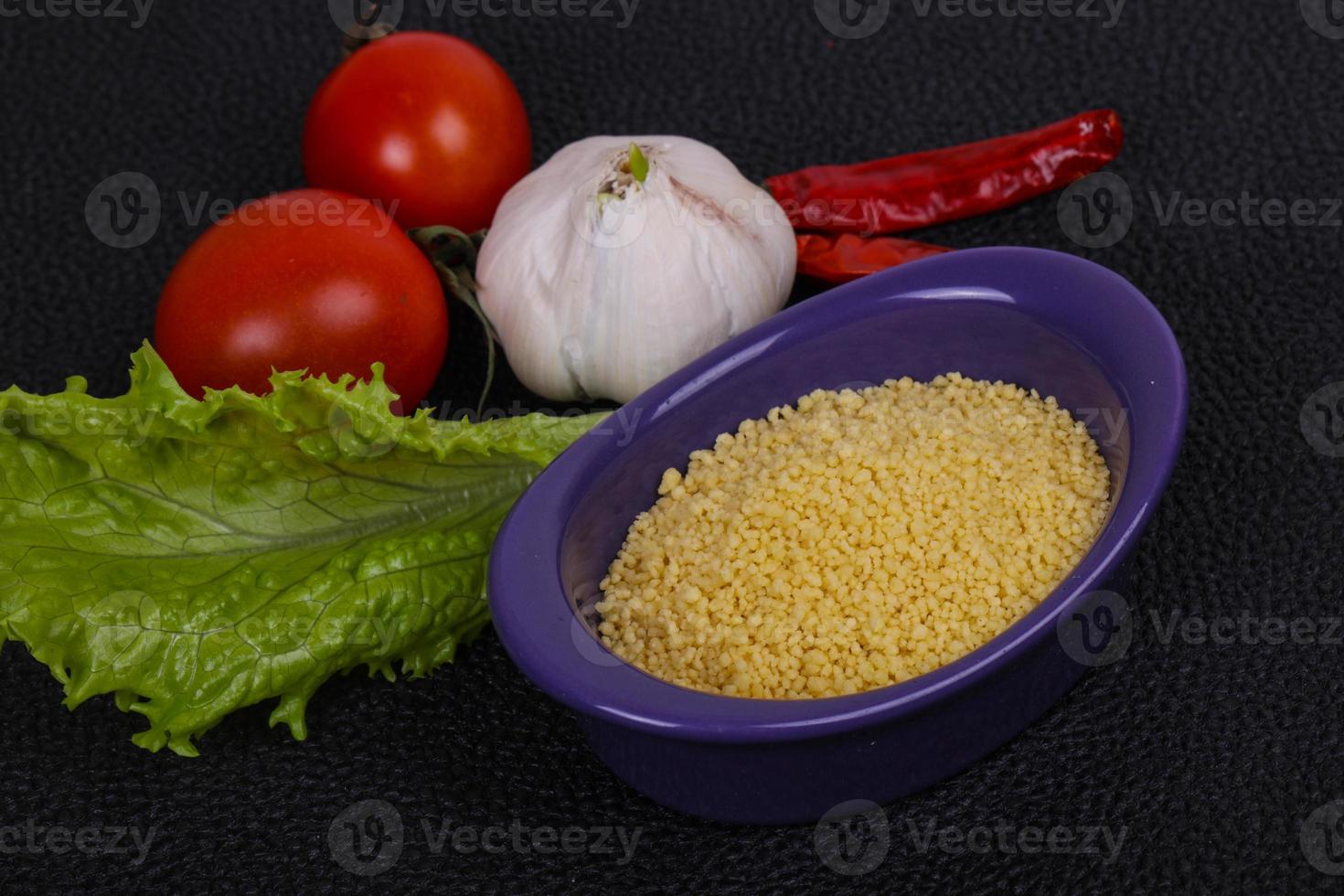 cous cous crudo nella ciotola servito con foglie di insalata, pomodoro e pepe foto