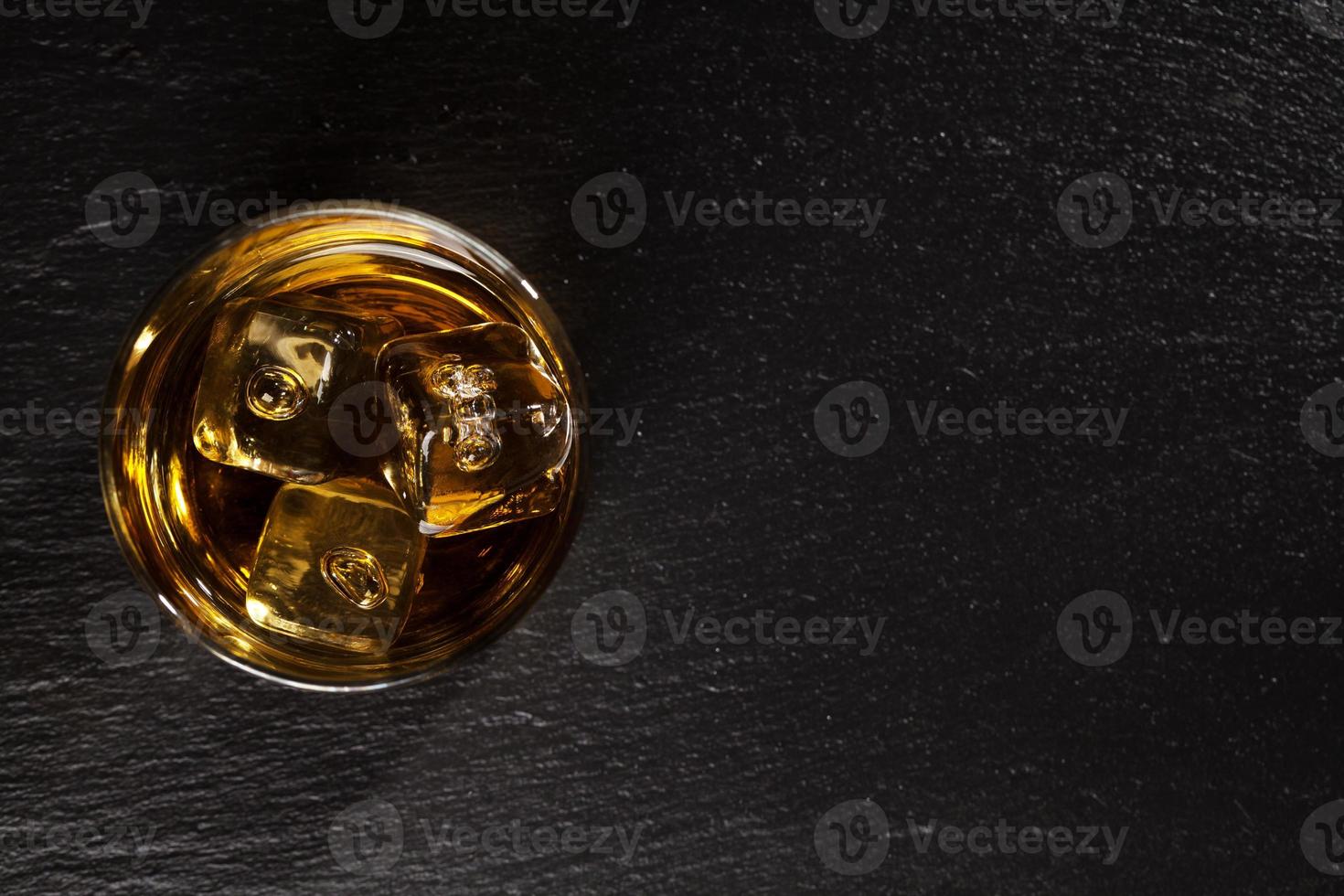 bicchiere di whisky con ghiaccio su pietra nera foto