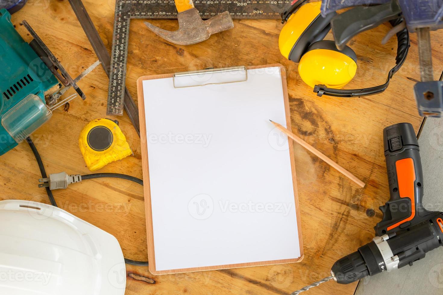 mockup appunti in bianco con foglio bianco e matita sul tavolo da falegname, caschi di sicurezza bianchi e attrezzi da lavoro sul banco da lavoro in falegnameria foto