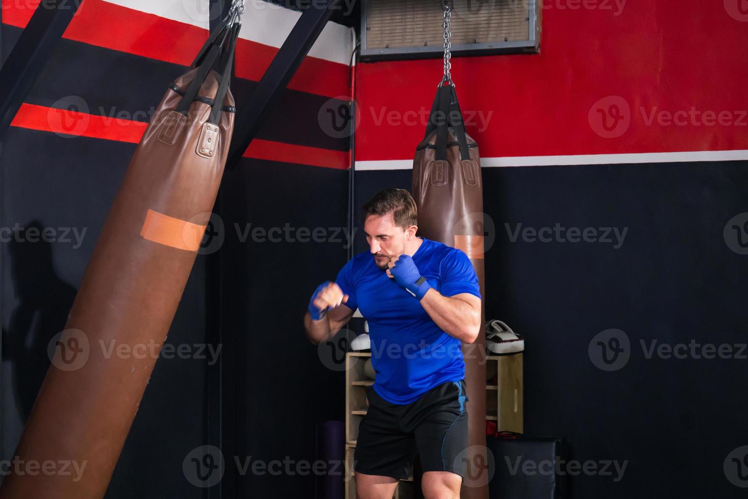 pugile uomo che esercita pugni con sacco da boxe in palestra, pugile che colpisce un sacco da boxe enorme in uno studio di boxe foto