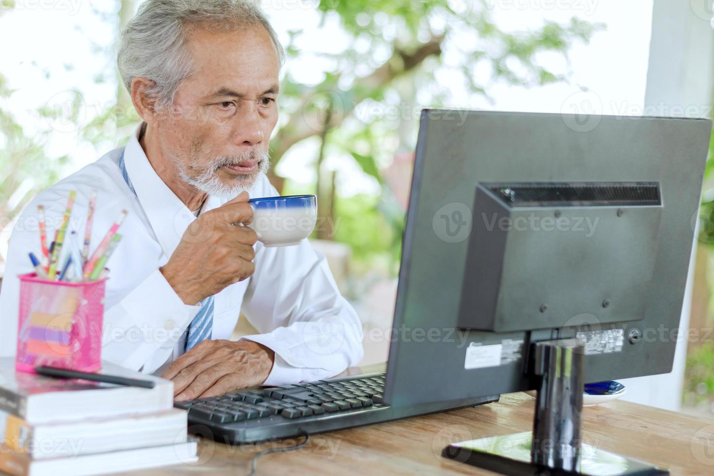 un anziano uomo d'affari con in mano una tazza di caffè davanti a un computer foto