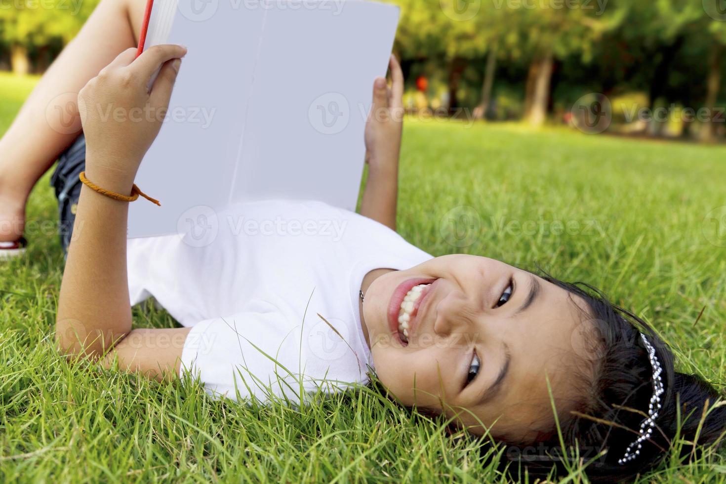 la bambina asiatica si rilassa e legge un libro nel parco foto