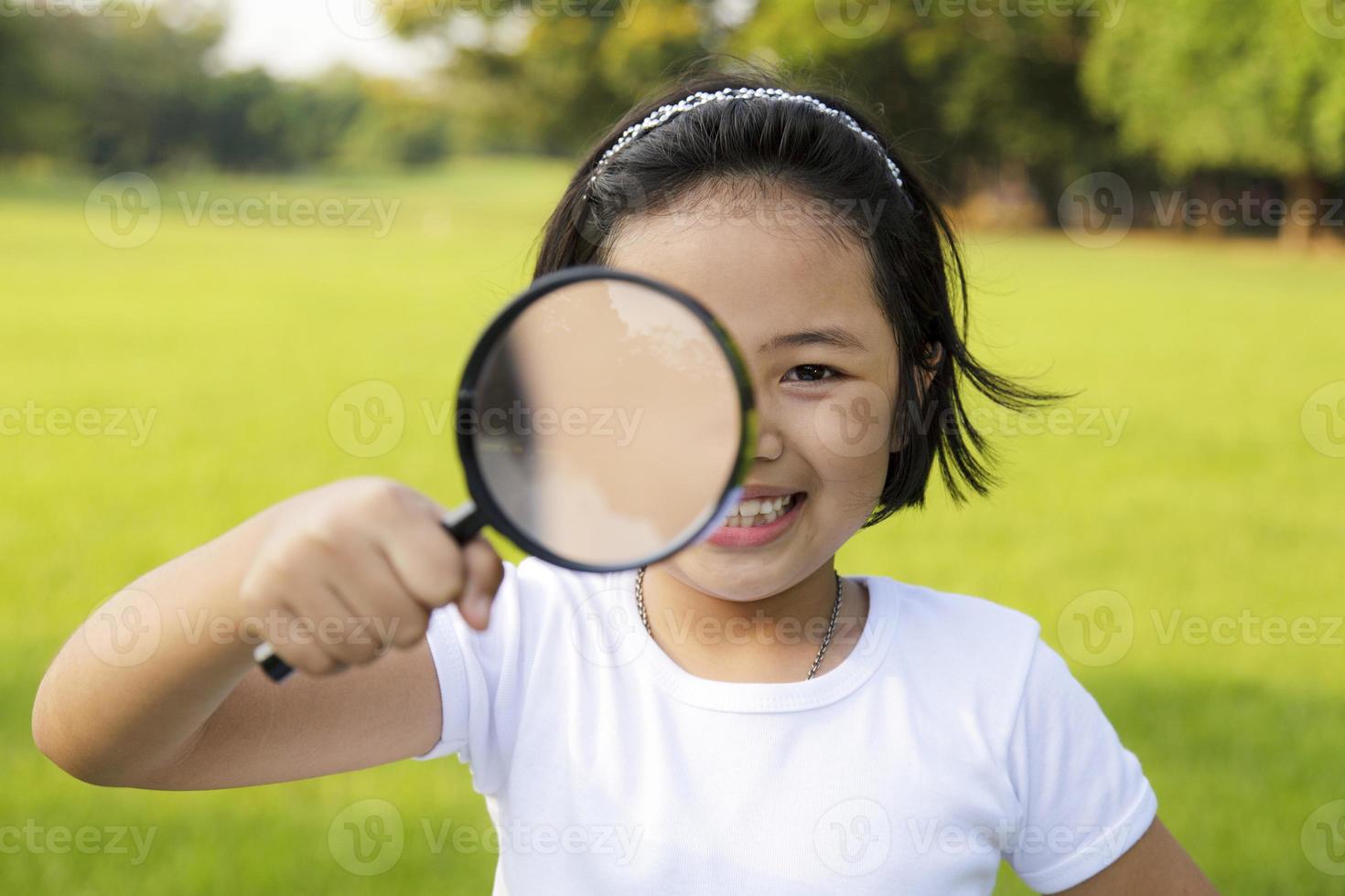 bambina asiatica che tiene una lente d'ingrandimento all'aperto foto