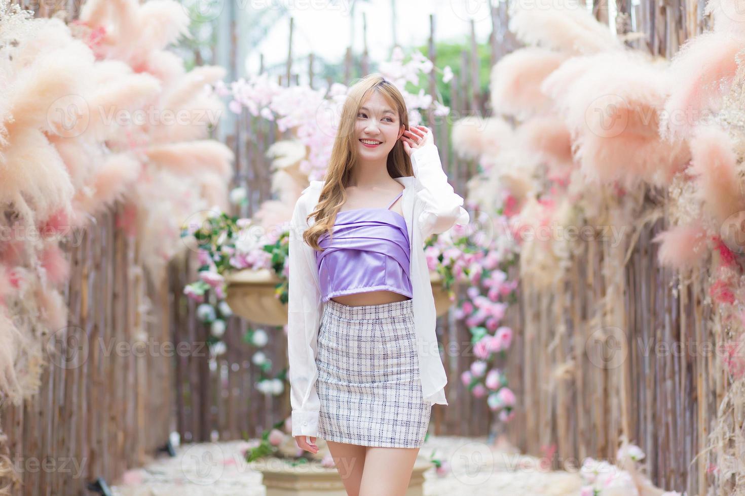 bella ragazza asiatica con lunghi capelli color bronzo che indossa una gonna corta e una manica lunga bianca si trova nel giardino del caffè. foto