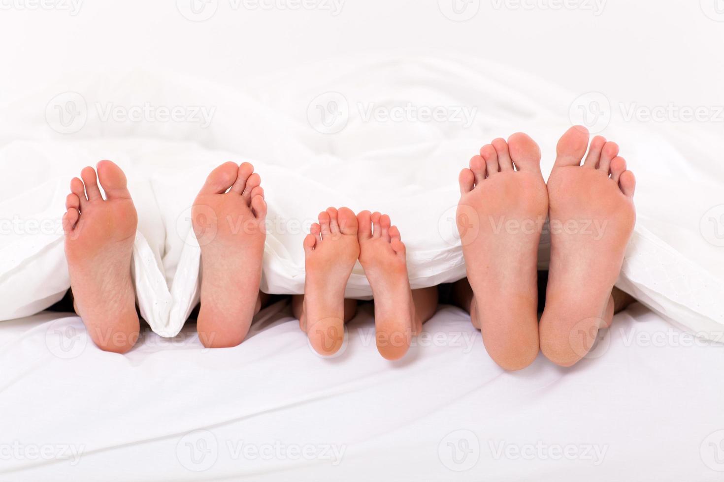 felice famiglia di tre persone sdraiata sotto il piumone foto