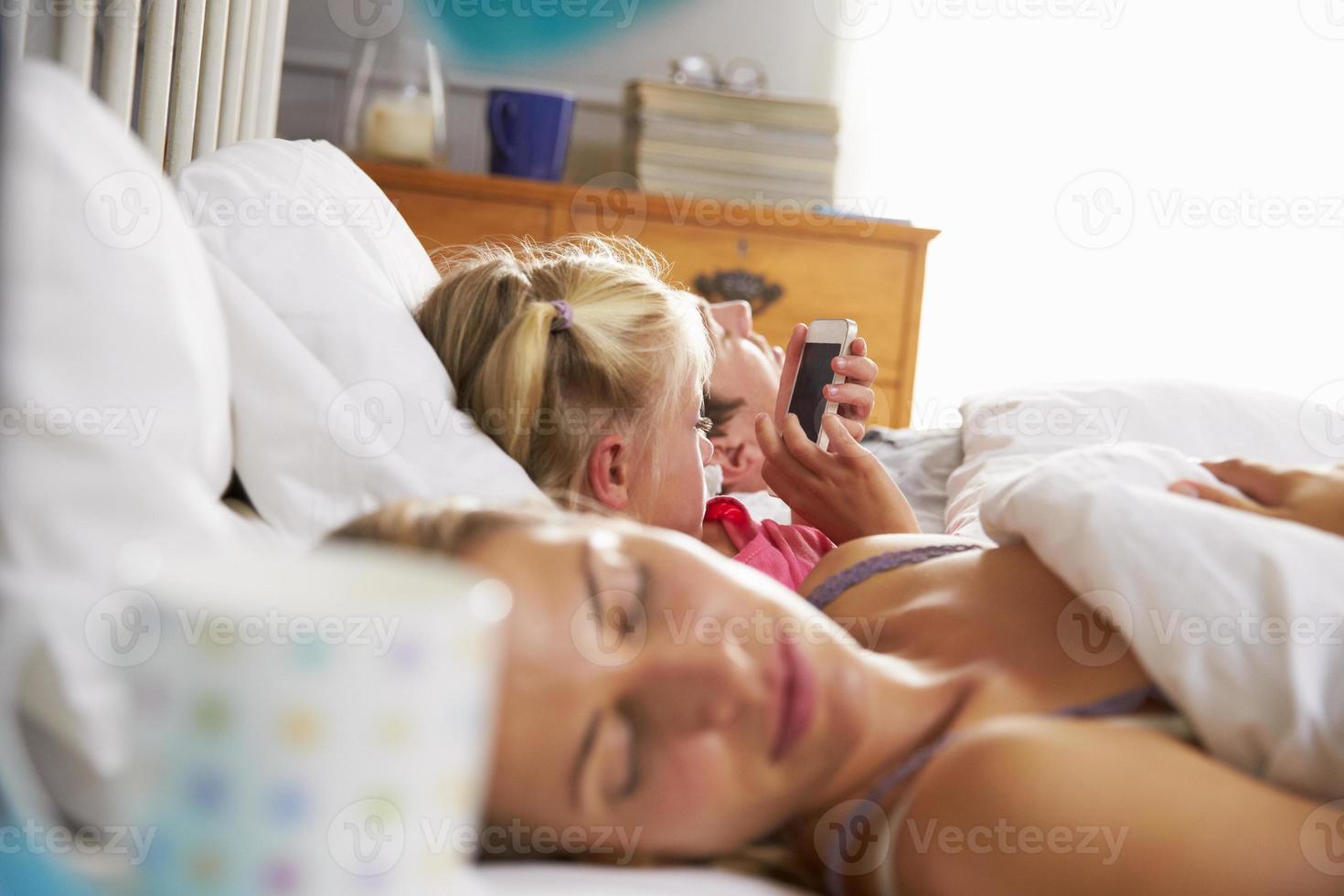 la figlia gioca con il cellulare a letto mentre i genitori dormono foto