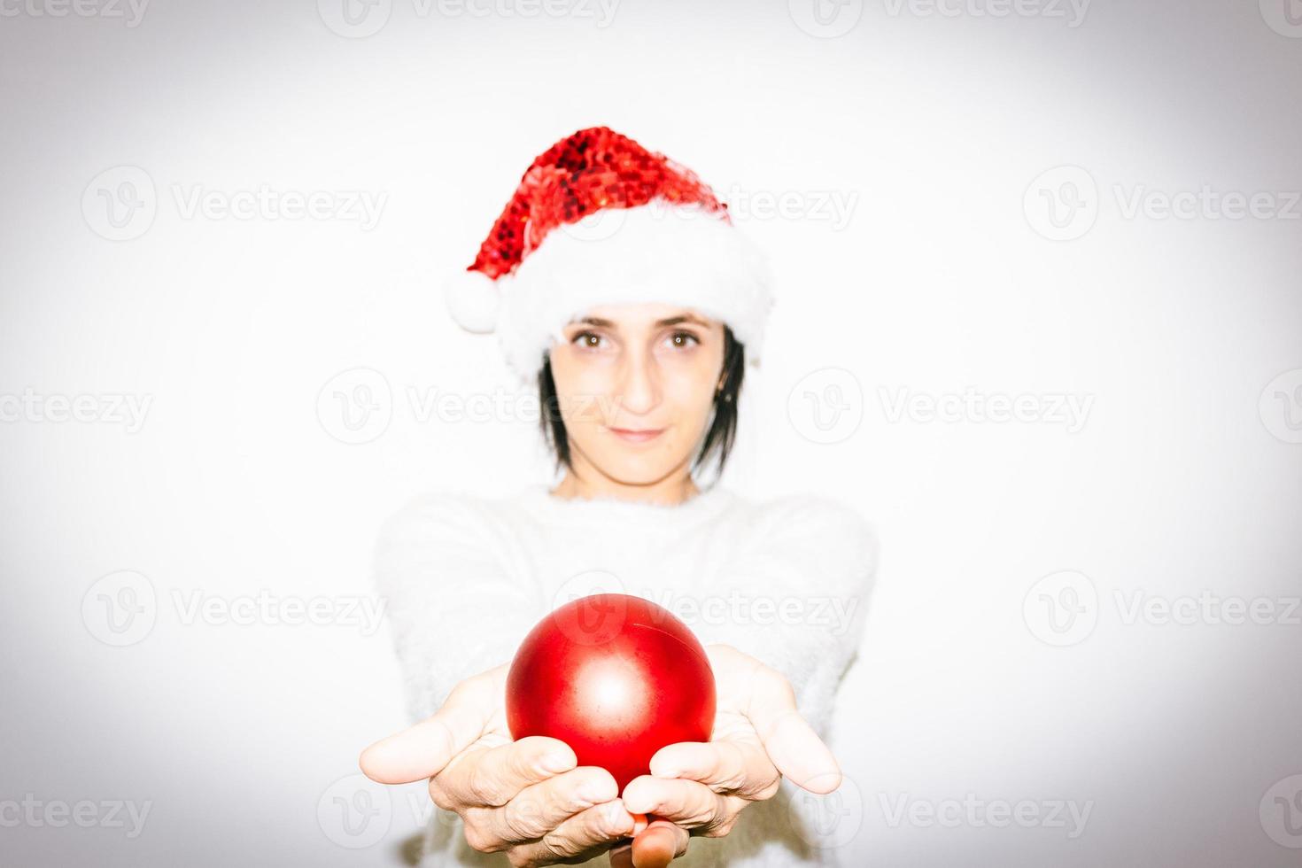 la donna in vestito di natale tiene in due mani il regalo della palla lucida della decorazione di natale rossa. felicità e condivisione di amore e speranza nelle celebrazioni foto