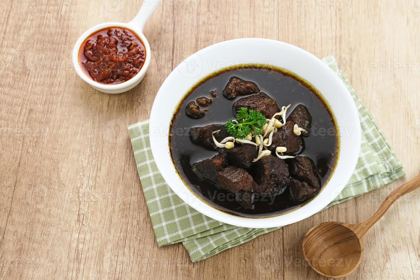 rawon, zuppa nera di manzo tradizionale indonesiana. servito su una ciotola con germogli di fagioli mung, pasta di peperoncino e uovo salato foto