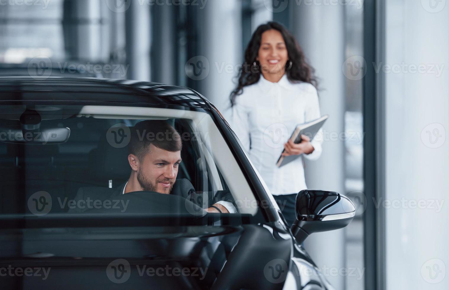 tutti sono soddisfatti. cliente maschio e donna d'affari moderna nel salone dell'automobile foto