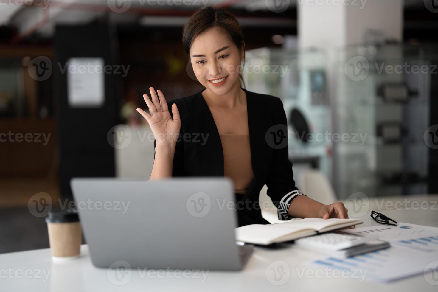 giovane donna d'affari asiatica che fa videochiamate sul laptop a casa, saluta lo schermo, chatta con clienti, colleghi. lavoro a distanza, freelance, docente online, insegnante foto