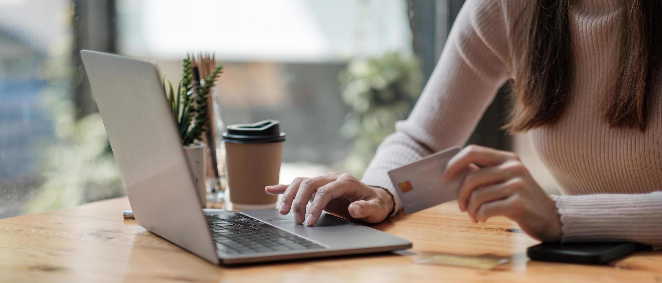 primo piano di una ragazza nera in possesso di una carta di credito bancaria e digita sul laptop, shopping online utilizzando il computer, acquisto di merci o ordinazione online, inserimento di conti bancari e dettagli nell'offerta bancaria online. foto