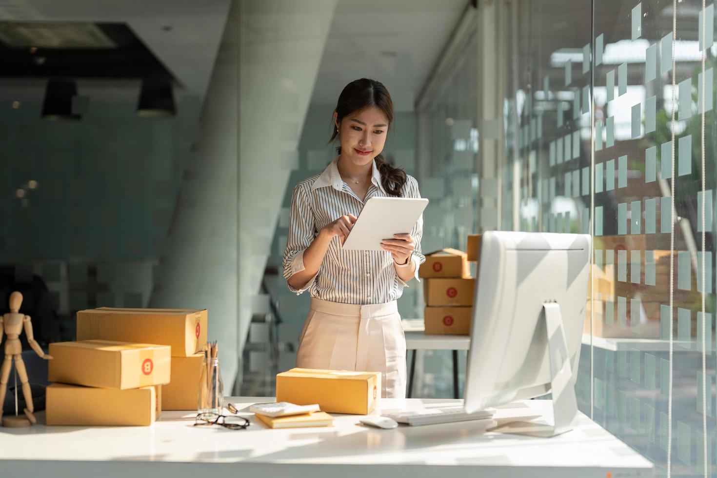 avviare il proprietario di una piccola impresa che lavora con la tavoletta digitale a casa. venditore freelance donna controlla l'ordine del prodotto, imballando le merci per la consegna. vendita online, e-commerce, concetto di spedizione foto