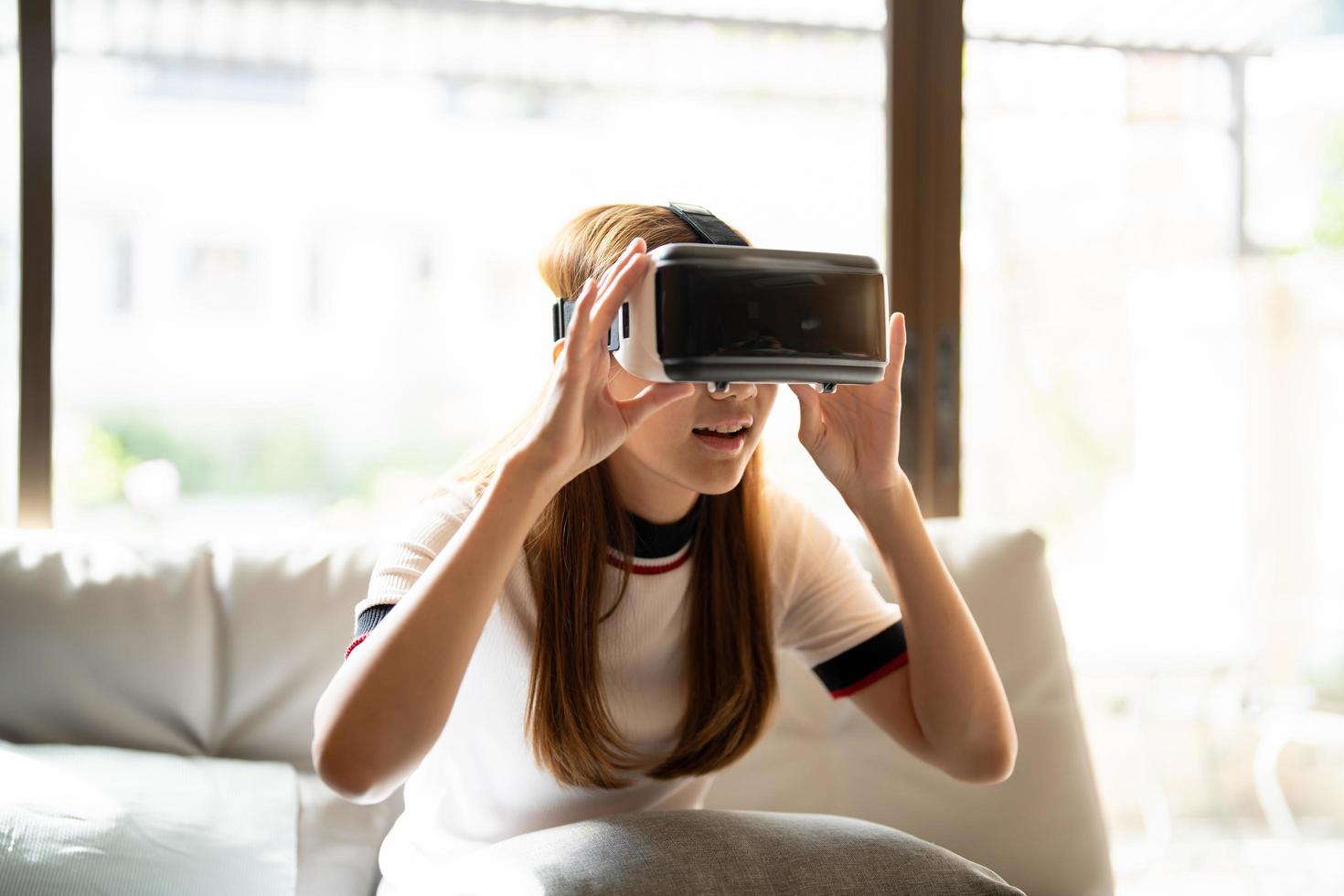 eccitare la donna asiatica che gioca online con occhiali vr e controller a casa sua foto