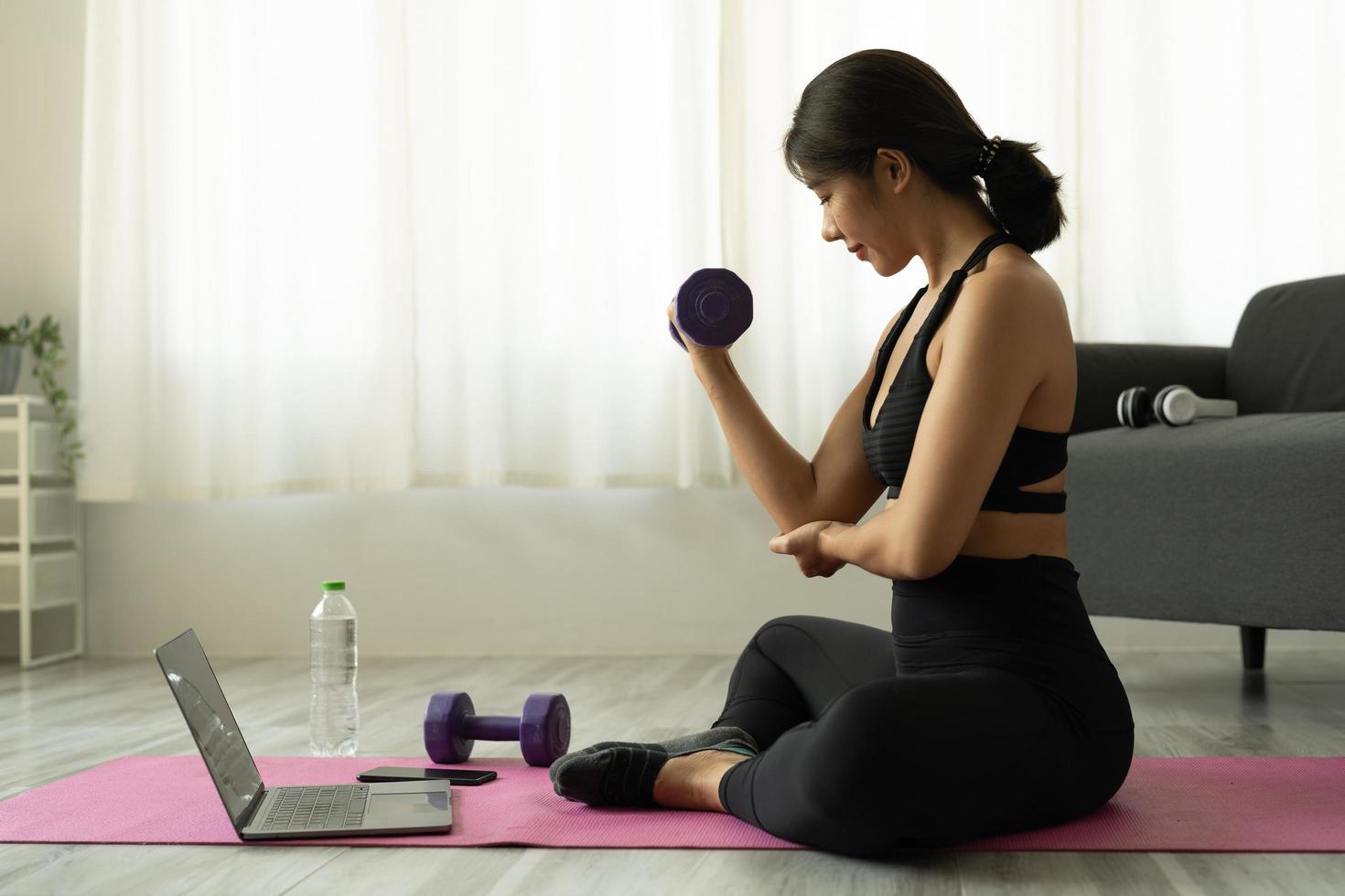 giovane donna asiatica che fa esercizi di fitness a casa attraverso la classe virtuale foto