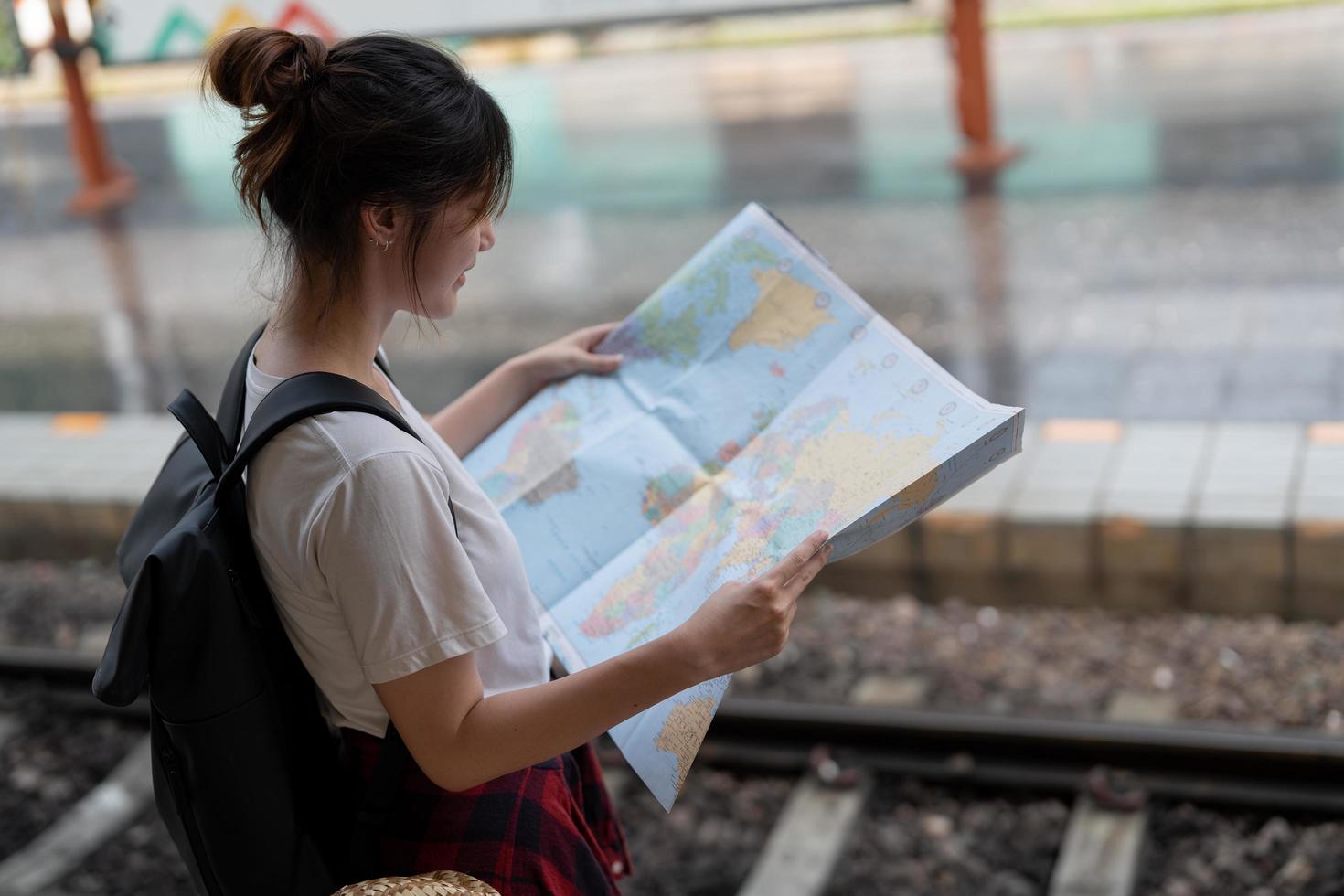 una giovane donna che viaggia in piedi con la mappa sceglie dove viaggiare e fa la valigia in attesa del treno alla stazione dei treni foto
