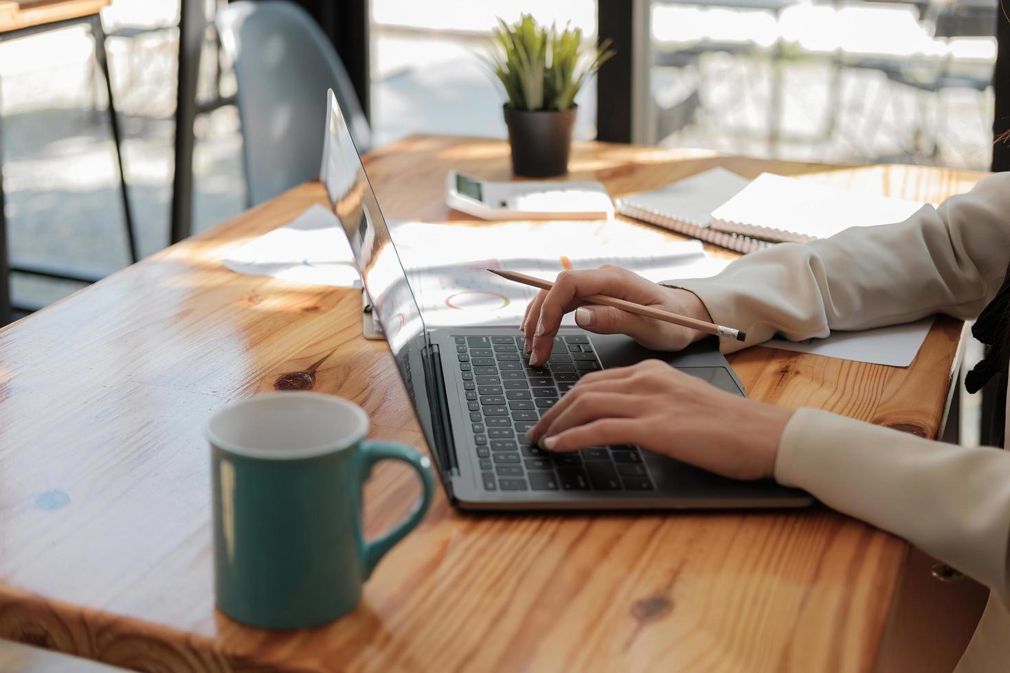 primo piano donna d'affari che utilizza un computer portatile per analizzare il rapporto sul bilancio finanziario dell'azienda e i costi di avanzamento del lavoro e pianificazione sulla scrivania in legno. foto