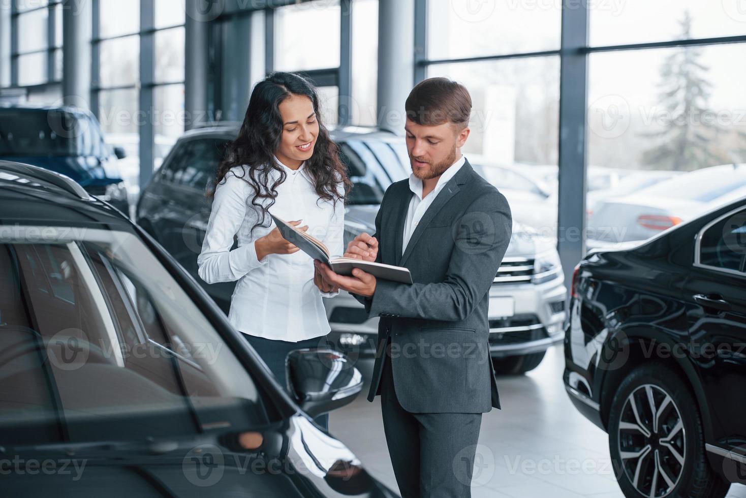 dove devo firmare cliente femminile e uomo d'affari barbuto moderno ed elegante nel salone dell'automobile foto