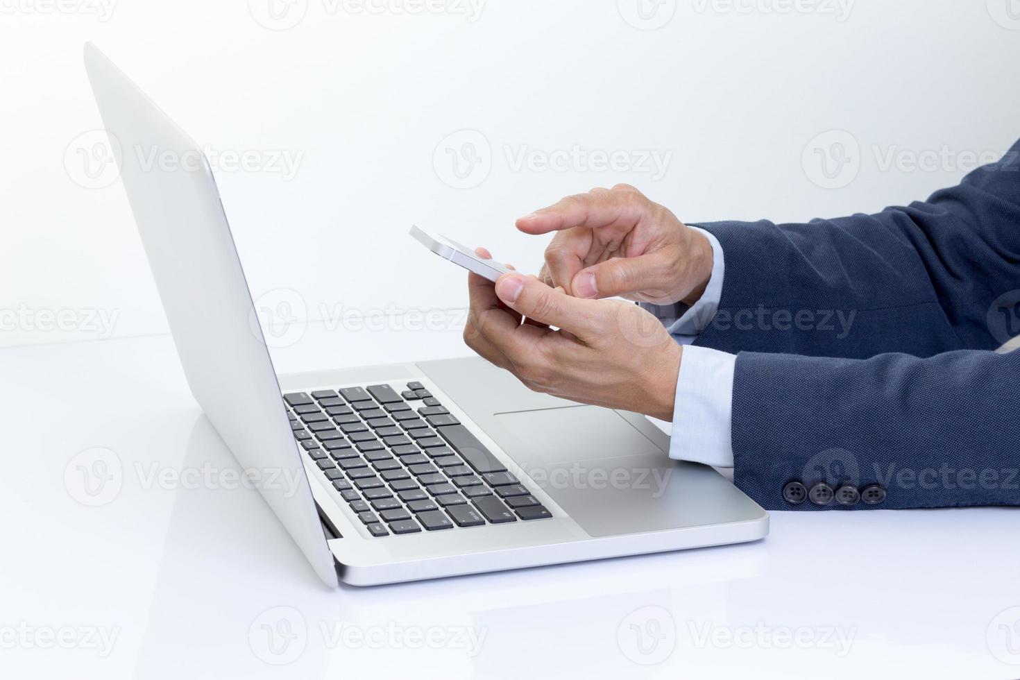 mani dell'uomo d'affari che tengono telefono cellulare con il computer portatile foto