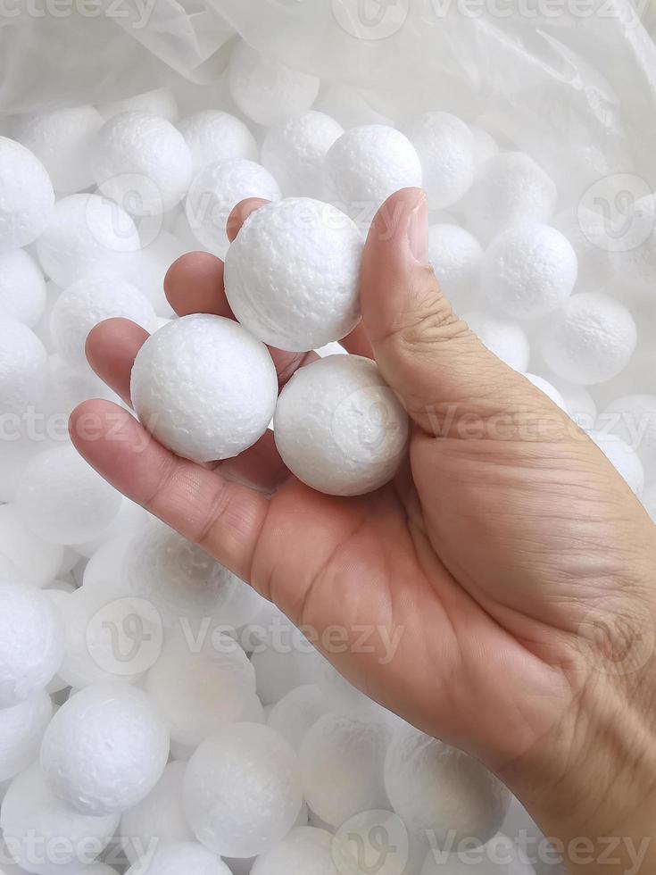 mano che tiene la palla di perline di schiuma di polistirene bianco caduta dalla macchina di polistirolo per scatola di imballaggio di roba fragile su sfondo blu moderno di lusso per la decorazione foto